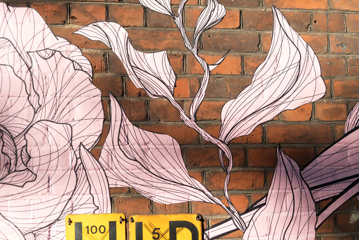 Exterior of a restaurant building, showing a detailed mural of flowers and plants flowing across the open brick face of the building. Mural by SAINT Design for mallow, a vegan restaurant in London.