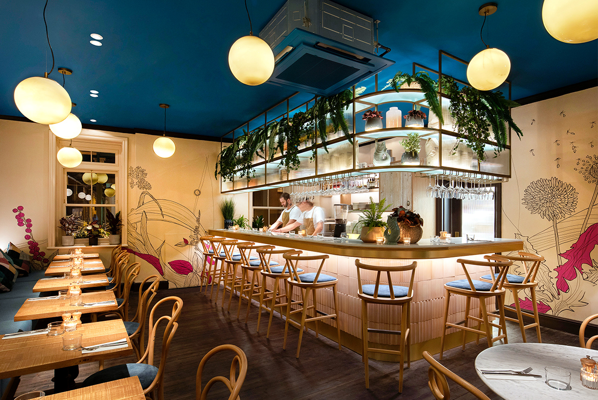Interior design of a restaurant, showing a bar and seating around it and a detailed mural of flowers and plants painted direct to the walls. Mural by SAINT Design for mallow, a vegan restaurant in London.