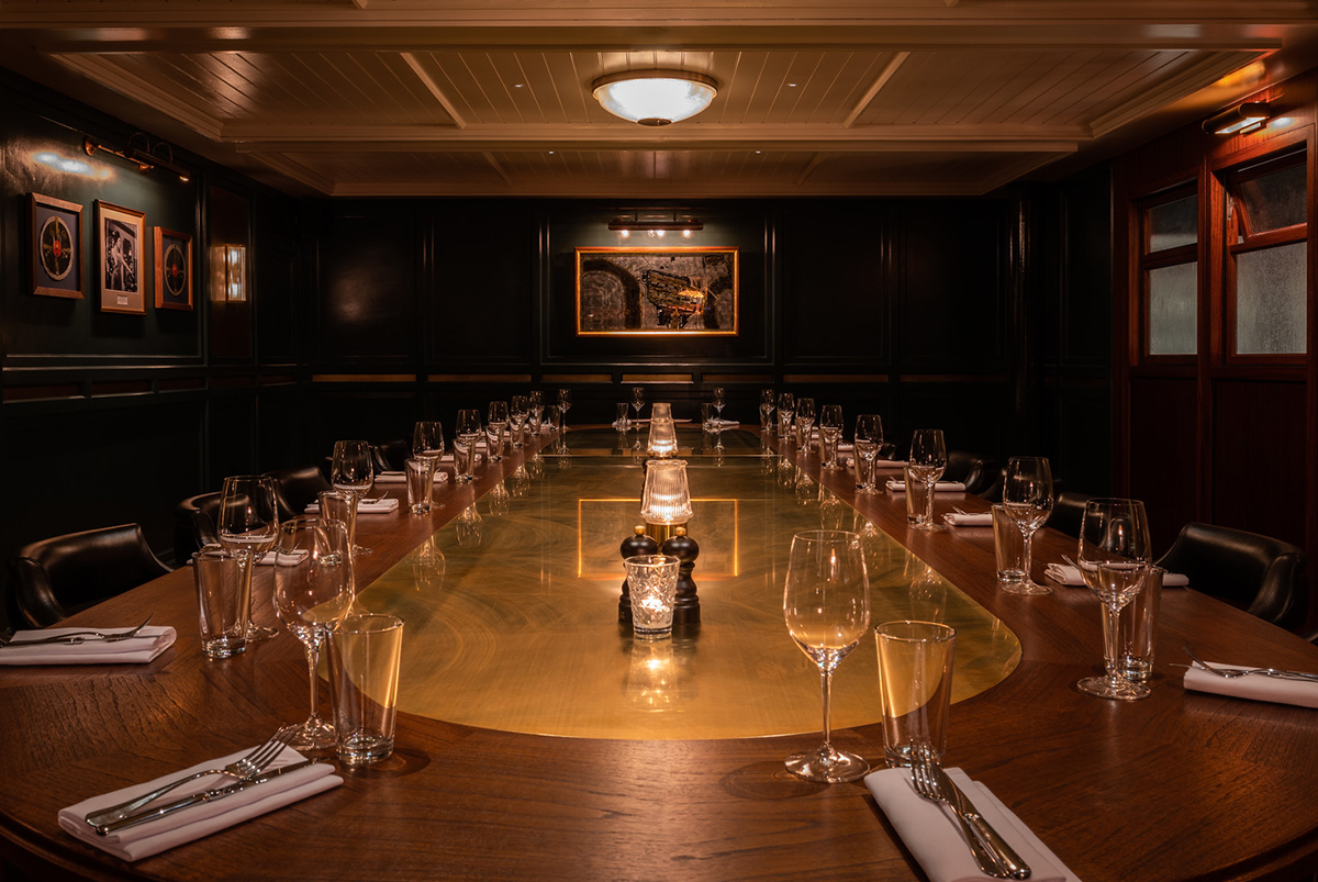 Photograph of the private dining room at Hawksmoor Wood Wharf showing the mirror art of a map of the Isle of Dogs at the end of the table, by SAINT Design for Hawksmoor.